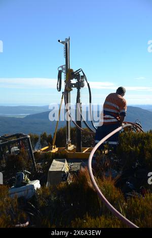 HAUPIRI, NUOVA ZELANDA, 7 MAGGIO 2024: I perforatori gestiscono un carro di perforazione portatile per affondare un foro di 10 metri sulla sommità del monte Morgan, affacciato sulla valle di Haupiri, West Coast, nuova Zelanda. Il foro verrà utilizzato per strumenti di monitoraggio GPS sismico per misurare il movimento lungo la faglia alpina che corre vicino alla base della montagna. Tutte le attrezzature di perforazione, tra cui un compressore d'aria, un generatore e un carro di perforazione, sono state portate in vetta in elicottero. Foto Stock