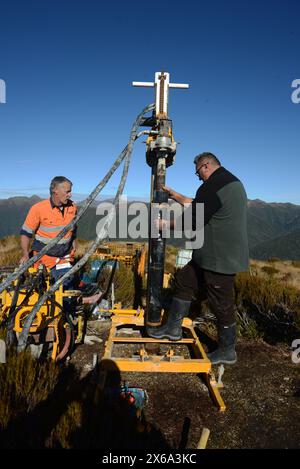 HAUPIRI, NUOVA ZELANDA, 7 MAGGIO 2024: I perforatori gestiscono un carro di perforazione portatile per affondare un foro di 10 metri sulla sommità del monte Morgan, affacciato sulla valle di Haupiri, West Coast, nuova Zelanda. Il foro verrà utilizzato per strumenti di monitoraggio GPS sismico per misurare il movimento lungo la faglia alpina che corre vicino alla base della montagna. Tutte le attrezzature di perforazione, tra cui un compressore d'aria, un generatore e un carro di perforazione, sono state portate in vetta in elicottero. Foto Stock