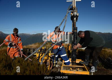 HAUPIRI, NUOVA ZELANDA, 7 MAGGIO 2024: I perforatori gestiscono un carro di perforazione portatile per affondare un foro di 10 metri sulla sommità del monte Morgan, affacciato sulla valle di Haupiri, West Coast, nuova Zelanda. Il foro verrà utilizzato per strumenti di monitoraggio GPS sismico per misurare il movimento lungo la faglia alpina che corre vicino alla base della montagna. Tutte le attrezzature di perforazione, tra cui un compressore d'aria, un generatore e un carro di perforazione, sono state portate in vetta in elicottero. Foto Stock