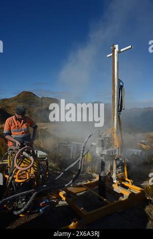 HAUPIRI, NUOVA ZELANDA, 7 MAGGIO 2024: I perforatori gestiscono un carro di perforazione portatile per affondare un foro di 10 metri sulla sommità del monte Morgan, affacciato sulla valle di Haupiri, West Coast, nuova Zelanda. Il foro verrà utilizzato per strumenti di monitoraggio GPS sismico per misurare il movimento lungo la faglia alpina che corre vicino alla base della montagna. Tutte le attrezzature di perforazione, tra cui un compressore d'aria, un generatore e un carro di perforazione, sono state portate in vetta in elicottero. Foto Stock