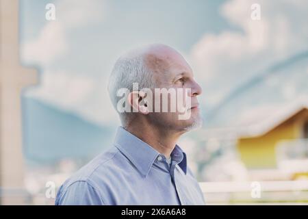 Un uomo di mezza età contempla il paesaggio sereno, un'espressione delicata che gioca sul viso sotto un cielo morbido Foto Stock