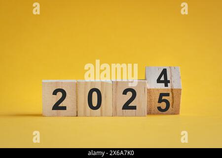 Dal 2024 al 2025, numeri su blocchi di legno. Su sfondo giallo, concetto di anno nuovo. Foto Stock