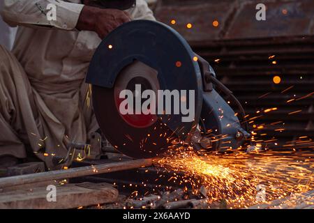 Saldatore che taglia tubi e aste metalliche nella sua officina stradale con taglierina elettrica Foto Stock