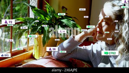 Immagine di icone dei social media su una donna anziana caucasica che guarda fuori dalla finestra a casa Foto Stock