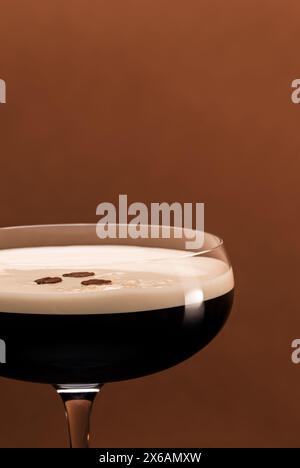 Cocktail espresso Martini servito in un elegante bicchiere coupé decorato con chicchi di caffè su sfondo color caffè. Foto Stock