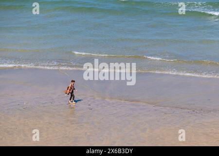 Una donna solitaria che cammina a piedi nudi attraverso la spiaggia Great Western GT Western sulla costa di Newquay in Cornovaglia nel Regno Unito. Foto Stock