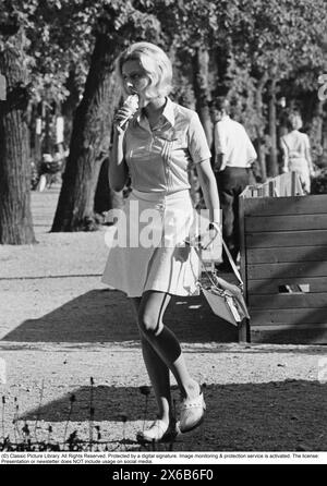 Giovane donna svedese che prende un gelato in una calda e soleggiata giornata estiva. Ha tipicamente anni '70 vestita con camicetta, gonna, borsa e zoccoli bianchi. 1970 Foto Stock