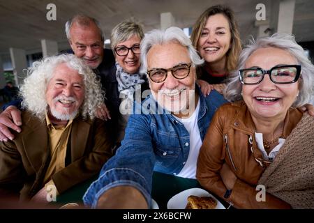 Felice uomo di capelli grigi maturo che scatta un selfie di anziani di gruppo amici caucasici allegri in posa insieme Foto Stock