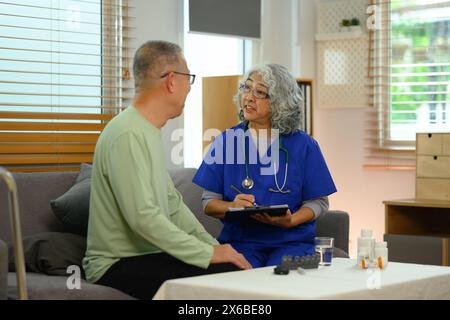 Medico in scrub blu che dà consulenza a paziente anziano presso la casa di cura Foto Stock