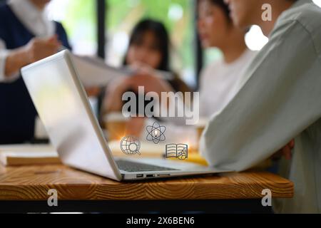 Primo piano di uno studente di collage che utilizza un laptop con nella libreria con varie icone Foto Stock