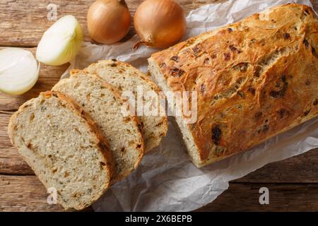 Pane alla cipolla appena sfornato, pane a fette, primo piano su pergamena su un tavolo di legno. Vista dall'alto orizzontale Foto Stock