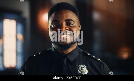 Autentico Ritratto di poliziotto nero felice e bello in uniforme universale sorridente alla fotocamera. Agente delle forze dell'ordine afroamericane di successo. Guardia di sicurezza del tribunale al lavoro. Foto Stock