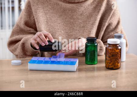 Donna che mette pillole e vitamine da prescrizione in un organizer giornaliero per pillole. Smistamento di integratori alimentari e antibiotici in pillole contai settimanali Foto Stock