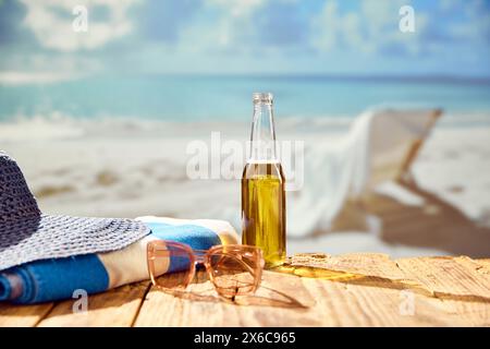 Rinfresco sulla spiaggia. Bottiglia di birra con cappello e asciugamano sulla spiaggia con splendida vista sull'oceano. Foto Stock