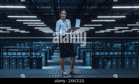 Ritratto di una donna ingegnere di data center che utilizza un computer laptop. Struttura specializzata in sala server con amministratore di sistema multietnico che lavora con Data Protection Network per la sicurezza informatica. Foto Stock