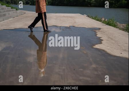 Primo piano delle gambe di una donna che cammina su una grande pozzanghera. Foto Stock