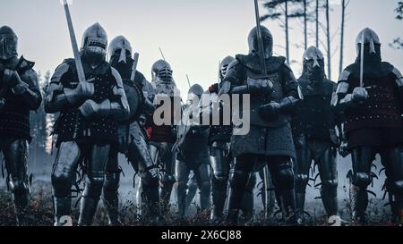 Epico esercito invasore dei Cavalieri medievali sul campo di battaglia. Soldati corazzati in caschi, con scudi e spade pronti per la battaglia. Guerra, conquista, crociata. Rievocazione storica. Foto Stock