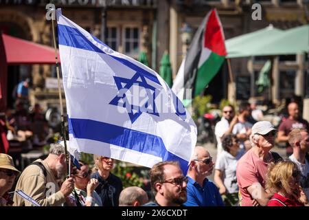 Brema, Germania. 14 maggio 2024. Una bandiera israeliana vola ad un raduno organizzato dalla società tedesca-israeliana Brema/Lower Weser per celebrare il giorno dell'indipendenza dello Stato di Israele sulla piazza del mercato di Brema, mentre le controdimostranti detengono una bandiera palestinese sullo sfondo. Diverse centinaia di persone avevano accettato l'invito a commemorare la fondazione dello Stato di Israele 76 anni fa. Crediti: Focke Strangmann/dpa/Alamy Live News Foto Stock