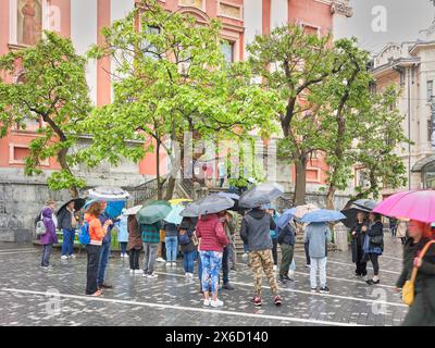 Turisti con ombrelloni in Piazza Preseren, fuori dalla chiesa francescana dell'Annunciazione, Lubiana, Slovenia, in una giornata di pioggia. Foto Stock