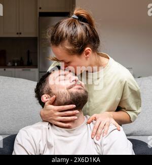 Felice giovane coppia adulta innamorata. Moglie che bacia suo marito a casa. Insieme e tenerezza. Foto Stock