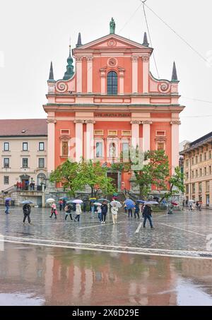 Turisti con ombrelloni in Piazza Preseren, fuori dalla chiesa francescana dell'Annunciazione, Lubiana, Slovenia, in una giornata di pioggia. Foto Stock