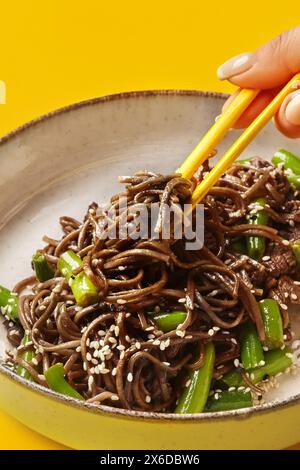 Donna che raccoglie spaghetti di soba di manzo con bacchette Foto Stock