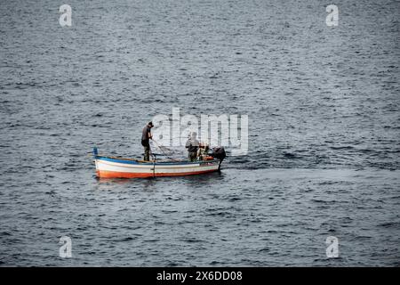 Due uomini che pescano da una piccola barca a motore al largo di Silicy, Italia, aprile 2024 Foto Stock