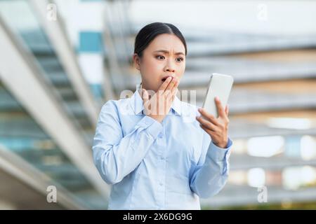 Sorpresa giovane donna che legge il messaggio sul suo smartphone in città Foto Stock