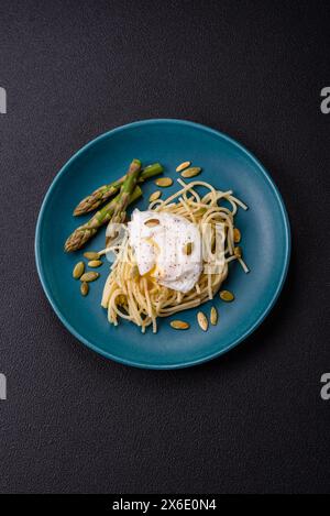 Colazione deliziosa e abbondante, con uova in camicia su pane tostato con formaggio spalmabile, asparagi, sale e spezie su sfondo di cemento scuro Foto Stock