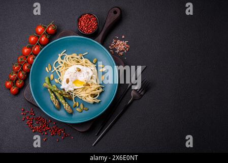 Colazione deliziosa e abbondante, con uova in camicia su pane tostato con formaggio spalmabile, asparagi, sale e spezie su sfondo di cemento scuro Foto Stock