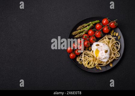 Colazione deliziosa e abbondante, con uova in camicia su pane tostato con formaggio spalmabile, asparagi, sale e spezie su sfondo di cemento scuro Foto Stock