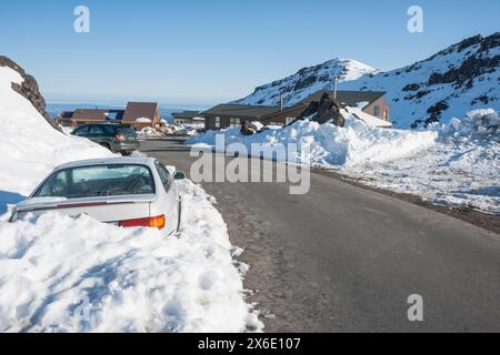 Strada che attraversa il campo da sci di Whakapapa con alloggio e veicoli nevicati sotto il cielo blu prima dell'inizio dell'azione al mattino. Foto Stock