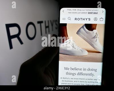 Persona che tiene un cellulare con la pagina web dell'azienda statunitense di scarpe e accessori Rothy's Inc. Davanti al logo. Messa a fuoco al centro del display del telefono. Foto Stock