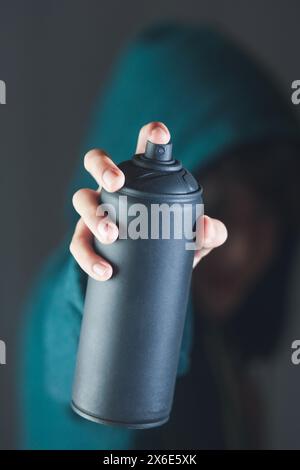 Una persona tiene in mano una bomboletta di vernice spray per graffiti. La lattina è nera e la persona indossa una felpa verde con cappuccio. La scena è un po' Foto Stock