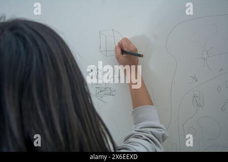 Una bambina irriconoscibile disegna forme geometriche sul muro Foto Stock