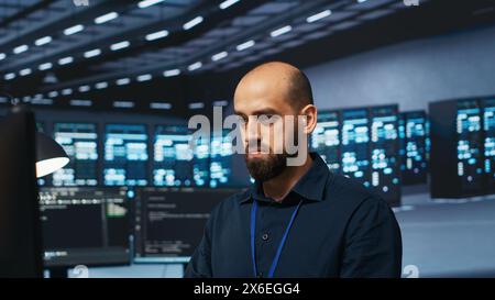 Programmazione informatica nella sala del data center che ospita blade server che memorizzano set di dati. Un professionista IT che scrive codice su PC per riparare i rack delle strutture di archiviazione dati che eseguono complesse operazioni di calcolo Foto Stock