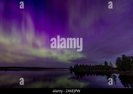 L'aurora boreale erutta sopra un lago nel Minnesota in un cielo buio sopra un brillante arcobaleno di luce Aurora Foto Stock