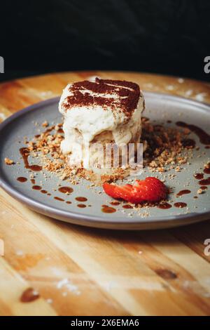 Delizioso tiramisù servito su un piatto di ceramica guarnito con fragole e cacao Foto Stock