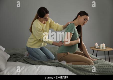 Doula massaggiava una donna incinta in camera da letto. Preparazione alla nascita del bambino Foto Stock