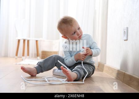 Bambino che gioca con la presa multipla vicino alla presa elettrica di casa. Situazione pericolosa Foto Stock