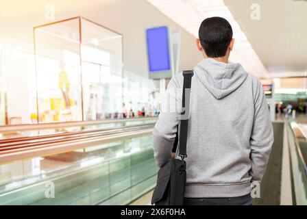 Ripresa da dietro di un giovane uomo irriconoscibile in piedi su una passerella in movimento nell'aeroporto Foto Stock
