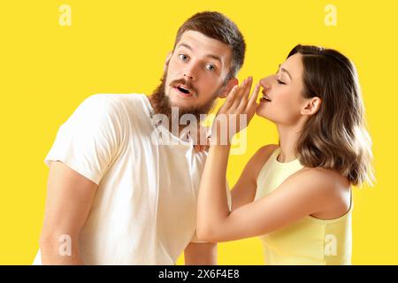 Una giovane donna sussurra all'orecchio del suo ragazzo su sfondo giallo Foto Stock