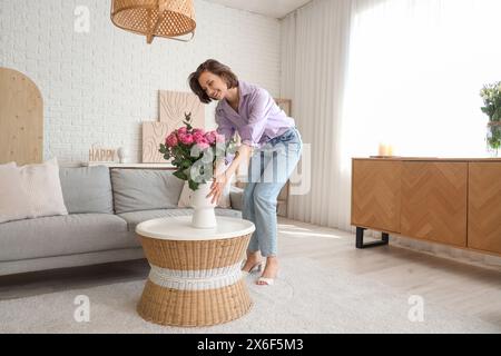 Giovane donna con rose rosa in vaso sul tavolo a casa Foto Stock