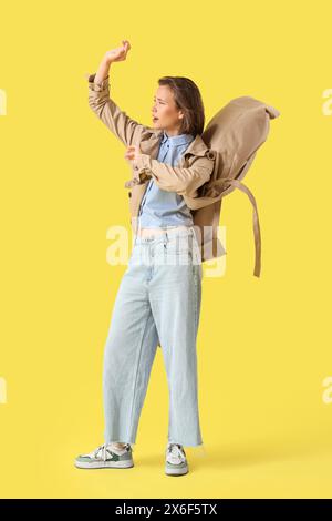 Giovane donna in cappotto con vento forte su sfondo giallo Foto Stock