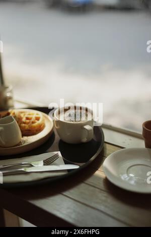 Tazza di caffè cappuccino e waffle con forchetta e coltello su un tavolo di legno contro il bokeh bg. Foto Stock