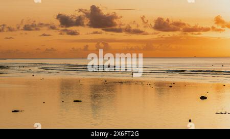 Sfumature dorate dipingono il cielo sulla spiaggia di Bingin, Bali, mentre il sole scende sotto l'orizzonte, proiettando un tranquillo bagliore sulle onde e sulle silhouette della sera Foto Stock
