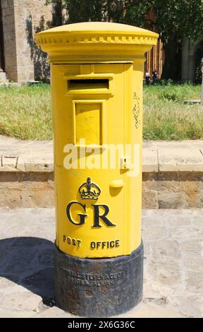 FAMAGOSTA, CIPRO DEL NORD - 08 MAGGIO 2024: Vecchia cassetta postale inglese d'epoca gialla con erba e sfondo a muro Foto Stock