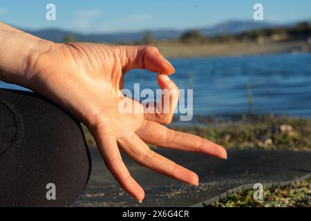 Mano di donna che fa il mudra di gyan in natura con un lago alle spalle Foto Stock