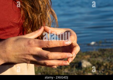 Mani di donna che fanno il mudra hakini in natura con un lago dietro Foto Stock