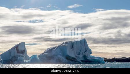 Un grande blocco di ghiaccio galleggia nell'oceano. Il cielo è nuvoloso e il sole splende attraverso le nuvole Foto Stock